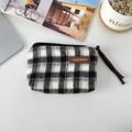 Flat lay of a checkered canvas coin purse with a leather logo on a desk with a plant - Woolen Black Gray Plaid