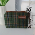 Close-up of a green plaid tweed coin purse with zipper and brand label on a desk - Woolen Green Plaid