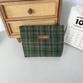 Detailaufnahme der grünen karierten Tweed-Kosmetiktasche mit Lederetikett auf Holztisch - Wolle Grün Karo