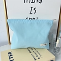 Detalle del neceser de lona azul claro con etiqueta de marca minimalista y cremallera - Azul