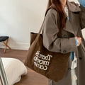 Dunkelbraune Canvas-Tragetasche mit weißem Schriftzug, am Model im Innenraum gezeigt - Shoulder Bag / Rotbrauner Leopard