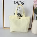 Detail of light yellow canvas tote bag showing the metal button closure and fabric texture - 8oz - Snap Button Style / Beige