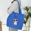 Close-up of bright blue canvas tote bag featuring embroidered pink cartoon pig and lettering - Royal Blue