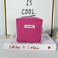 Close-up of pink canvas makeup bag with zipper and May Rabbit label on a book - Rose Red