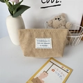 Detailopname van beige corduroy make-uptas met zachte stoftextuur en minimaal merklabel - Abrikoos