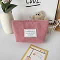 Detail of pink corduroy makeup bag with white fabric label in a cozy home setting - Nude Pink