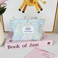 Detail of soft blue plush cosmetic bag with a white woven label on a pastel pink background - Blue Daisy