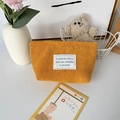 Detail van gembergele corduroy make-uptas met wit label in een gezellige huiselijke setting - Gembergeel