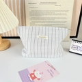 Close-up of pleated striped makeup bag with brand tag and metal zipper on desktop - Small Grey Plaid