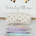 Detail of striped cream makeup bag featuring red heart embroidery and woven brand label - Pencil Case