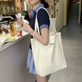 Minimalist off-white canvas tote bag with black typography shown in a cafe setting - Off-white