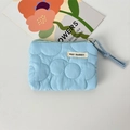 Détail macro d'une pochette matelassée bleu ciel avec motifs floraux et étiquette en tissu - Fleur Matelassée Bleue