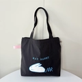 Detail of a black canvas tote bag featuring a white rabbit patch and blue embroidery - Black Lying Rabbit