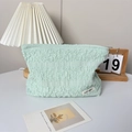 Detail of light green pleated fabric makeup bag with brand label on a wooden desk - Green
