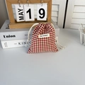 Close-up of red and white plaid drawstring pouch with logo label on stack of books - Red Check