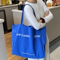 Minimalist large blue canvas tote bag with white lettering shown on shoulder by model - Royal Blue
