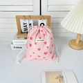 Pink drawstring bag with red hearts and May Rabbit label on a cozy desktop - Medium