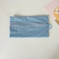 Detail view of sky blue grid nylon pouch featuring a contrast pink zipper with round pull ring - Blue
