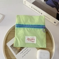 Detailed view of a mint green nylon mini pouch with a purple ring zipper on a wood tray - Green