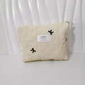 Close-up of quilted cosmetic bag featuring black bow embroidery and metal zipper - Handbag Creamy White