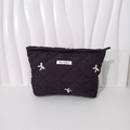 Detailed view of black quilted cosmetic bag featuring white bow embroidery and top zipper - Makeup Bag Black