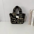 Dettaglio della borsa in peluche con motivo paisley ed etichetta su sfondo bianco - Totem nero etnico