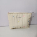 Close-up of quilted cream cosmetic bag with colorful heart embroidery and fabric label - Off-white Heart Embroidered Cosmetic Bag