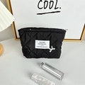 Macro view of black quilted makeup bag featuring logo tag and delicate white embroidery - Lipstick Bag Black