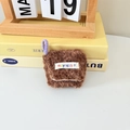 Close-up of brown plush AirPods case featuring a colorful mayrabbit woven label and strap - Brown