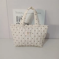 Gros plan du sac fourre-tout matelassé blanc avec motifs cœurs et étiquette logo - Sac à main blanc cassé