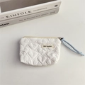 Detail view of white quilted heart pattern pouch with a woven puller on a clean background - White
