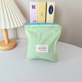 Close-up of light green nylon mini bag with blue zipper and colorful brand label - Vertical Style / Green