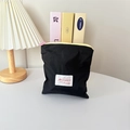 Macro shot of black nylon pouch with pink zipper and white woven label on white table - Vertical Style / Black