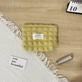 Detail of yellow quilted bubble fabric makeup bag with white label on a cozy surface - Bubble Yellow