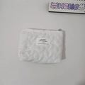 Detail shot of white quilted heart pattern and embroidered label on a compact pouch - White