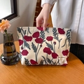 Florale Kosmetiktasche mit rotem Mohnblumenmuster und gewebtem Label auf Holztisch - Mohnblume