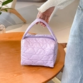 Close-up of light purple quilted cosmetic bag with heart patterns on a wooden table - Purple
