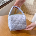 Detail of light purple quilted handbag with unique bear pattern stitching on a wood table - Blue