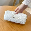 Dettaglio dell'astuccio trapuntato bianco con motivo a cuore e etichetta su tavolo legno - Bianco