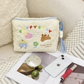 Nahaufnahme der cremefarbenen herzgesteppten Tasche mit Stickerei neben Make-up auf Sofa - PUPPY BABY Thema Aufbewahrungstasche