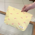 Detail van de geel geruite make-uptas met roze strikken en een merklabel in de hand - Geel Geruit