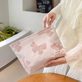 Rosa Jacquard-Kosmetiktasche mit Schmetterlingsmuster und Markenlabel in der Hand - Rosa Hintergrund Schleife