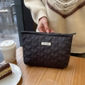 Detail of black quilted heart texture makeup bag held by hand in a cozy cafe setting - Black