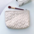 Dettaglio borsa da trucco trapuntata a cuore crema con etichetta May Rabbit sul tavolo - Cachi