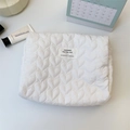 Close-up of white quilted heart pattern makeup bag with branded label on desk - White