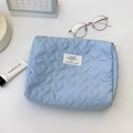 Close-up of light blue quilted cosmetic bag with heart pattern and minimalist branding - Blue