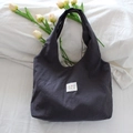 Détail d'un sac cabas en toile bleu marine à pois avec étiquette tissée sur draps blancs - Petit Pois Gris Foncé