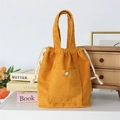 Close-up of yellow corduroy handbag featuring drawstring closure and blue button detail - Turmeric