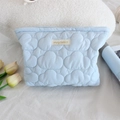 Detail of light blue quilted cosmetic bag with puffy cloud texture and brand woven label - Makeup Bag / Light Blue