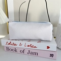 Close-up of white seersucker pencil case with blue zipper and metal pull on books - White